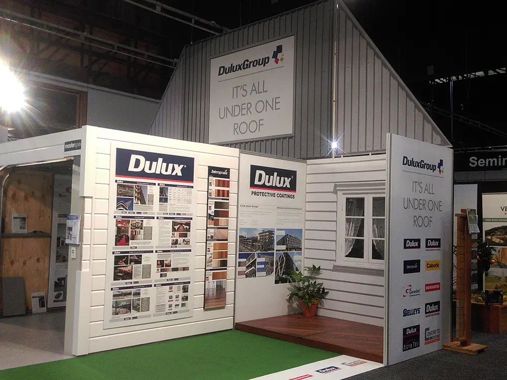 DuluxGroup stand built as a weatherboard house with corrugated gable, timber deck and artificial lawn