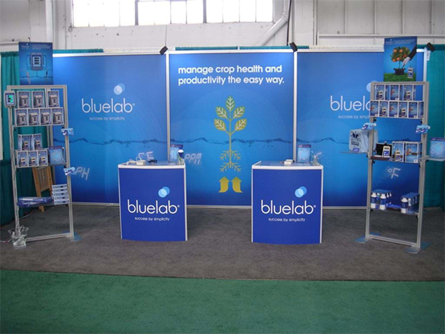Exhibition stand built on a modular aluminium post-and-rail frame, with three blue printed graphic panels, two branded counters and two metal brochure towers
