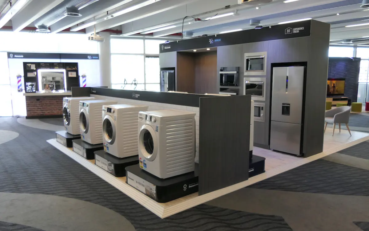 Panasonic washing machines on individual plinths beside a kitchen-style wall of built-in ovens