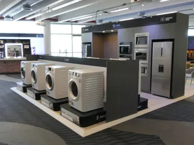 Panasonic front-loading washers on low plinths before a wall of built-in ovens and a fridge