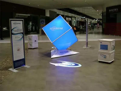 Large illuminated Sensodyne cube balanced on its corner with banners and a lit floor logo