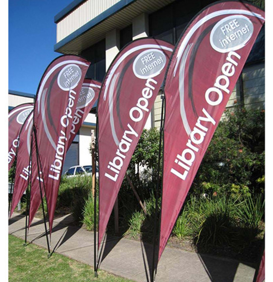 A row of maroon teardrop flags reading "Library Open" and "Free Internet" along a garden bed outside a building