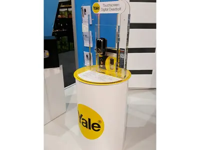 Yale digital deadbolt and packaging in a clear acrylic upright on a yellow-topped plinth