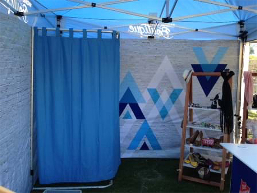 Inside a branded marquee with a printed back wall, a curtained change area and a timber shoe and accessories rack on artificial turf