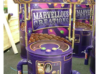 Row of Cadbury Marvellous Creations game stations with coloured buttons, gears and a Joyville sign