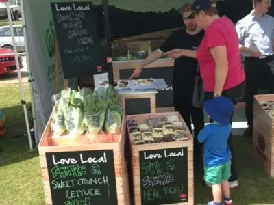 Woolworths Love Local crates of Sweet Crunch lettuce with chalkboard fronts beside a salad table