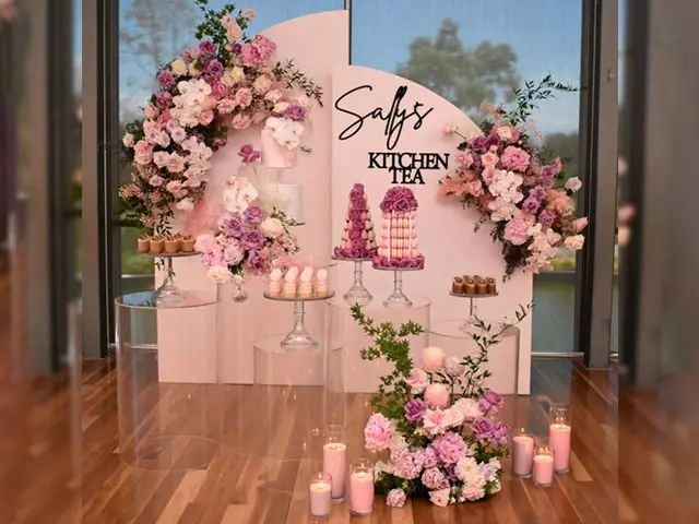 Dessert table with pale arched backdrop panels, cut-out lettering and clear plinths under cake stands