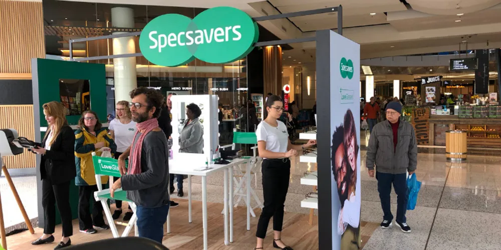 Specsavers kiosk in a shopping centre walkway with staff and freestanding graphics