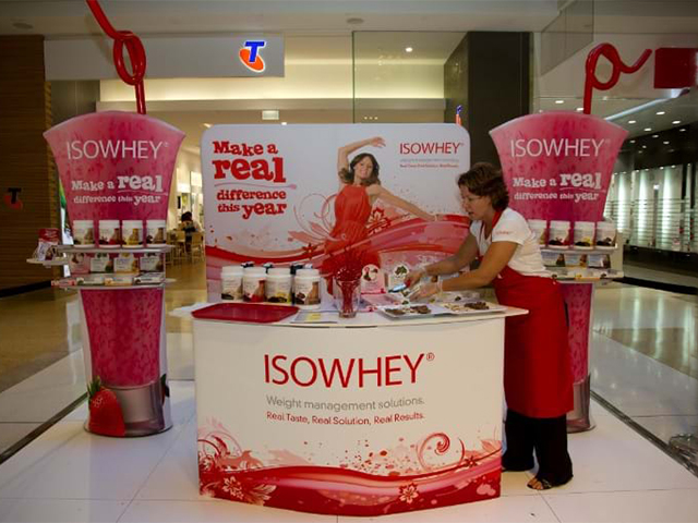 ISOWHEY sampling counter between two oversized smoothie-cup towers with product tubs on shelves