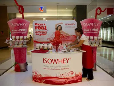 ISOWHEY sampling counter between two oversized smoothie-cup towers with product tubs on shelves