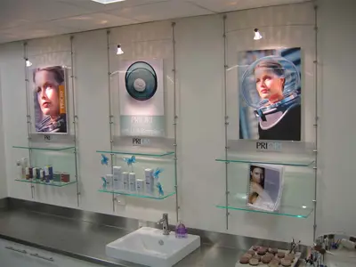 PRIORI skincare wall with spotlit image panels above glass shelves hung on slim cables