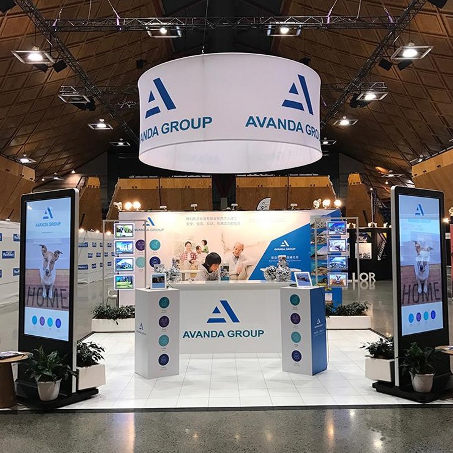 Round fabric banner suspended above an exhibition stand with a white counter, two plinths and two portrait digital screens