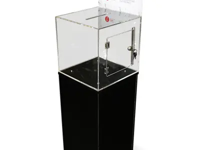 Clear acrylic donation box with a 'Donate Here' sign, raised on a tall black plinth