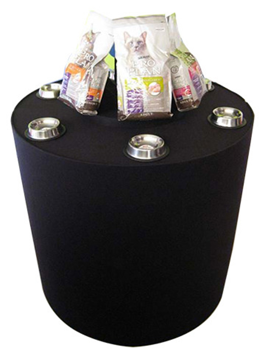 Round plinth with a black fabric cover, Pro Plan cat food packs on top and steel feeding bowls set into the top surface