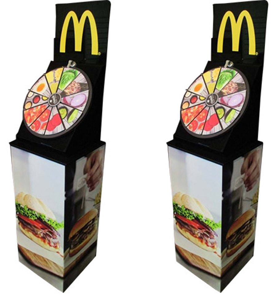 Two prize wheels set in angled housings on printed plinths, with McDonald's branding and ingredient-photo segments