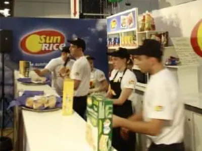 SunRice staff serving food samples from a long white exhibition counter at an expo