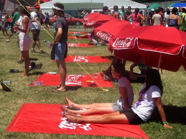 Red Coca-Cola mats and large red umbrellas spread across a grassy festival field