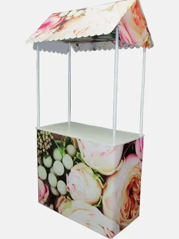 Rose-print demo table with a scalloped pitched roof on slim white posts